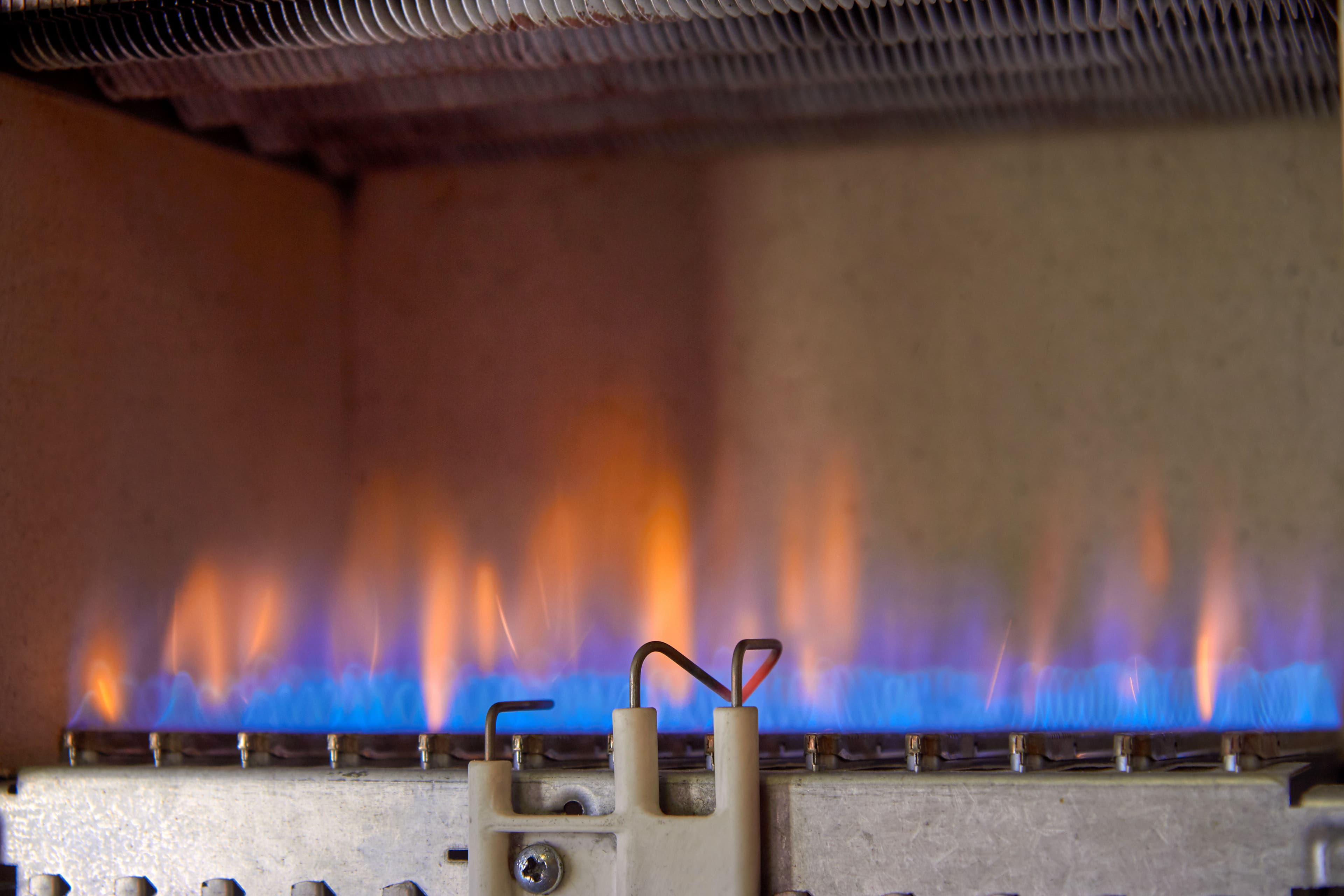 Close-up of a gas burner with blue and orange flames in a heating system.