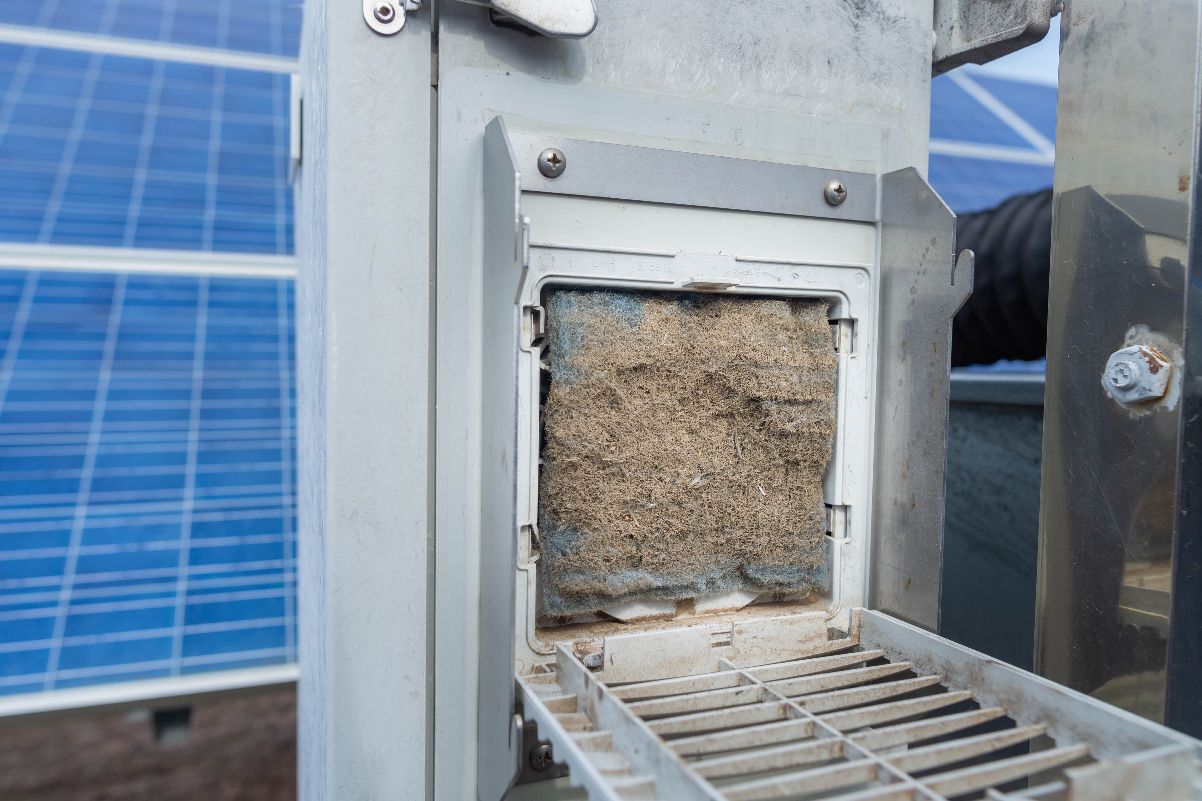 Dirty solar panel inverter filter showing dust accumulation, with solar panels in background.