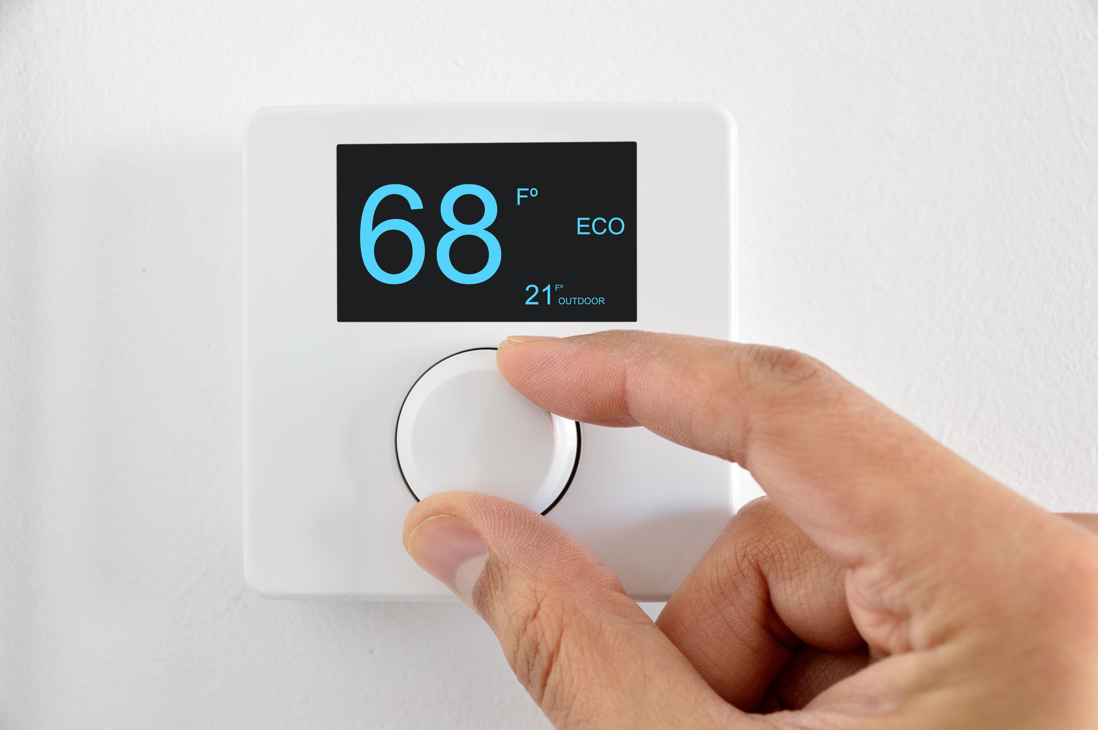 Smart thermostat displaying 68°F with a hand adjusting the temperature dial.