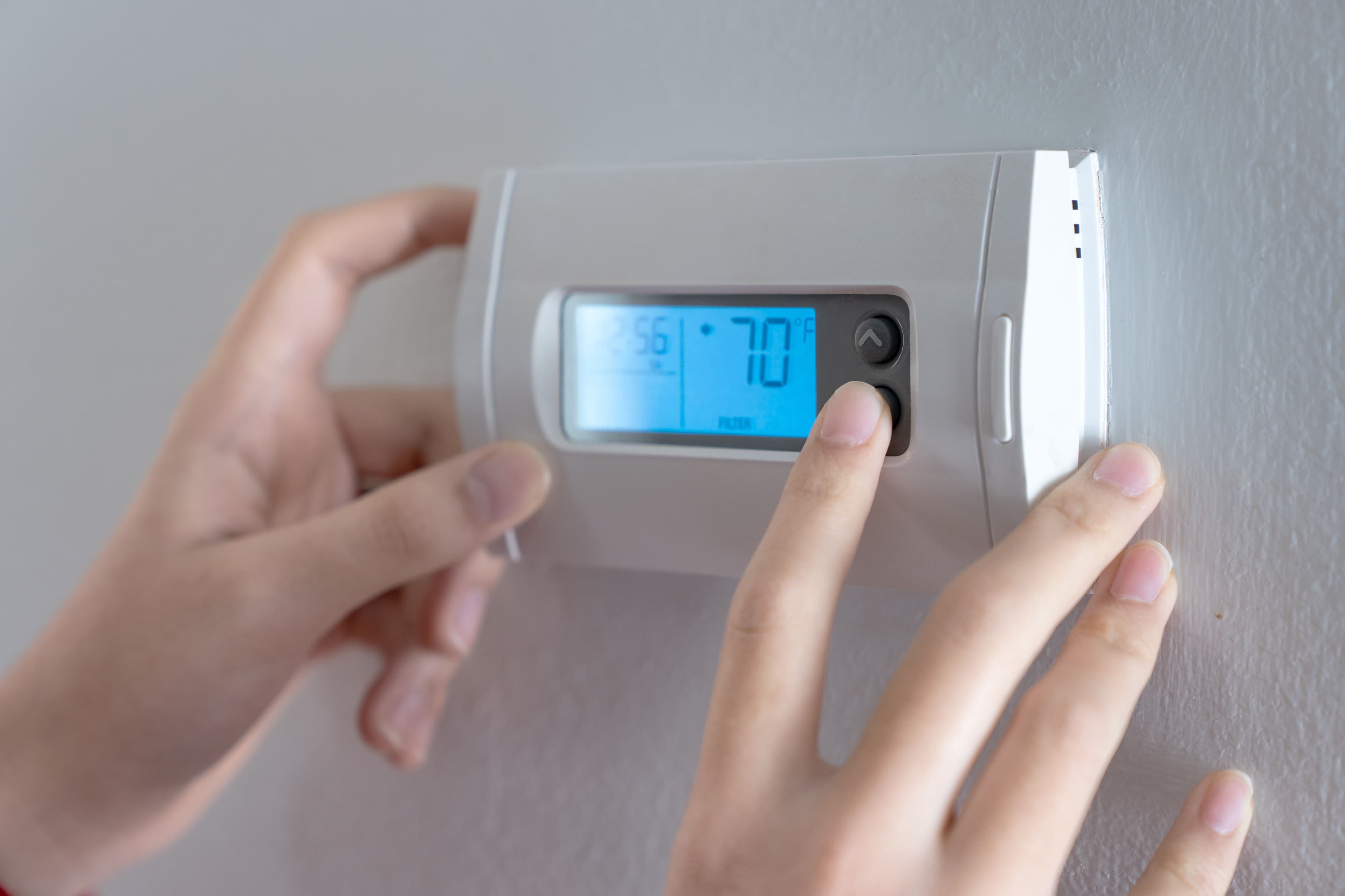 Person adjusting a digital thermostat to set temperature at 70 degrees Fahrenheit.