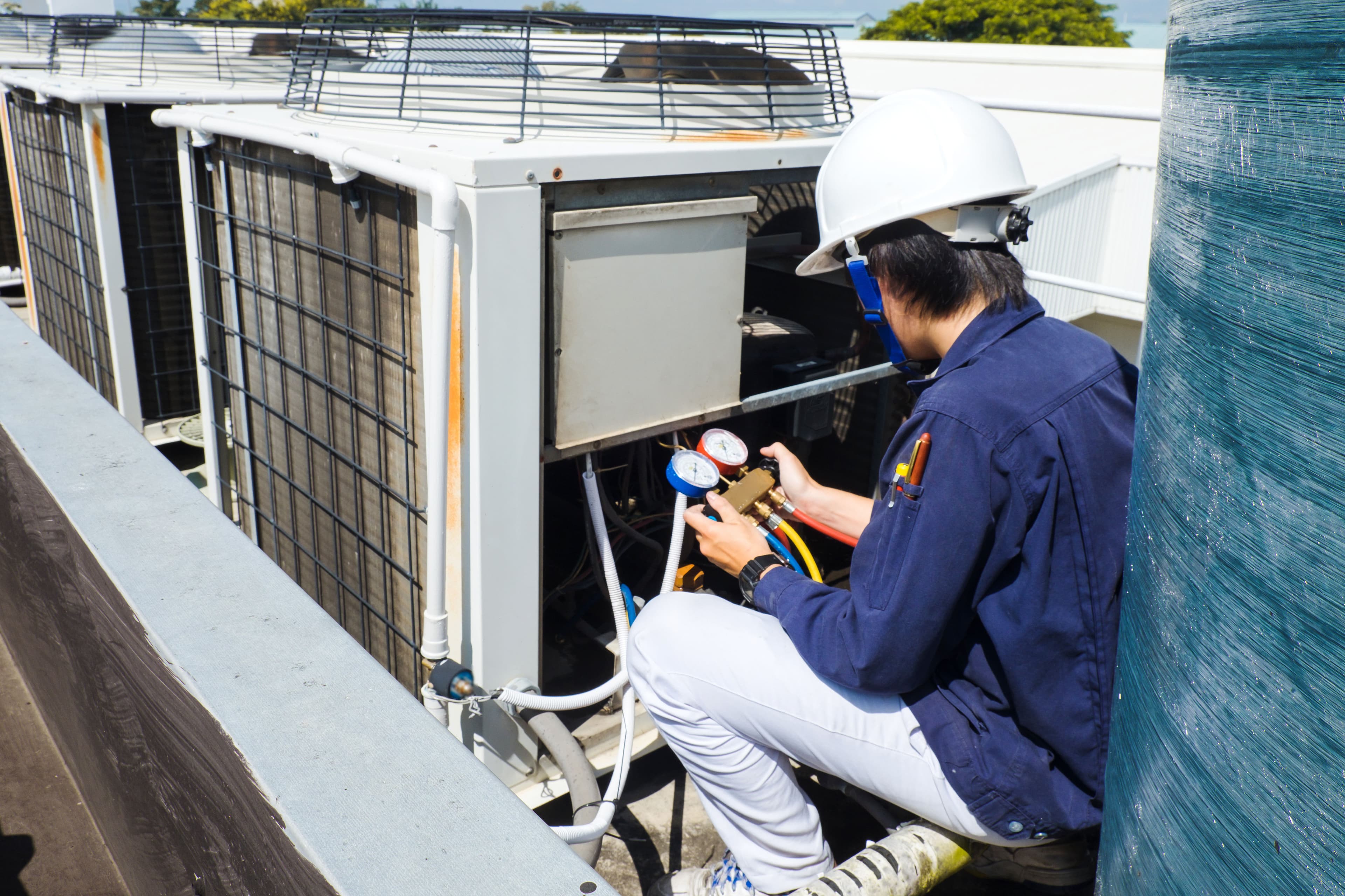 HVAC technician measuring pressure on air conditioning unit's gauges on rooftop.