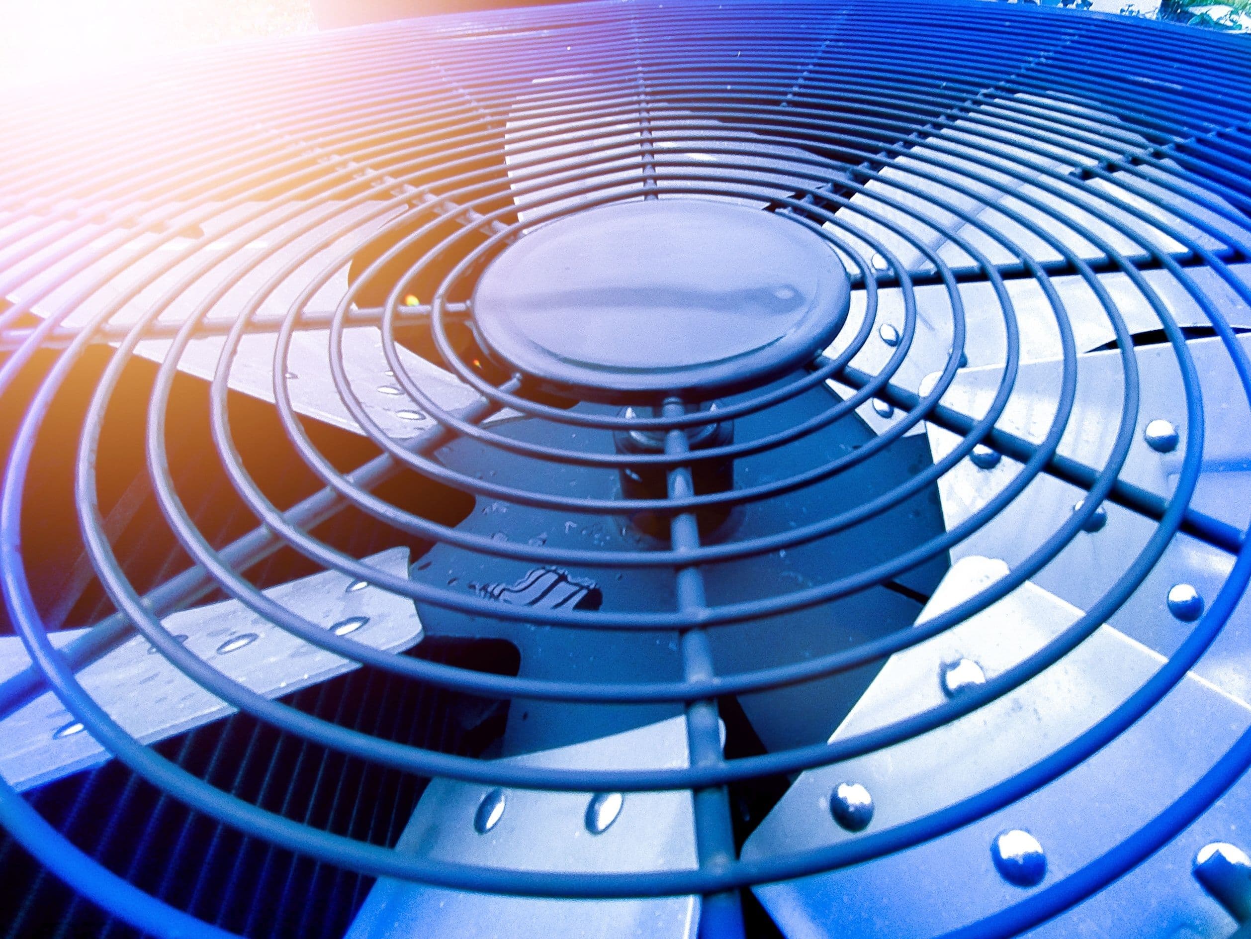 Close-up of an outdoor air conditioning unit fan with protective grills and cooling fins.