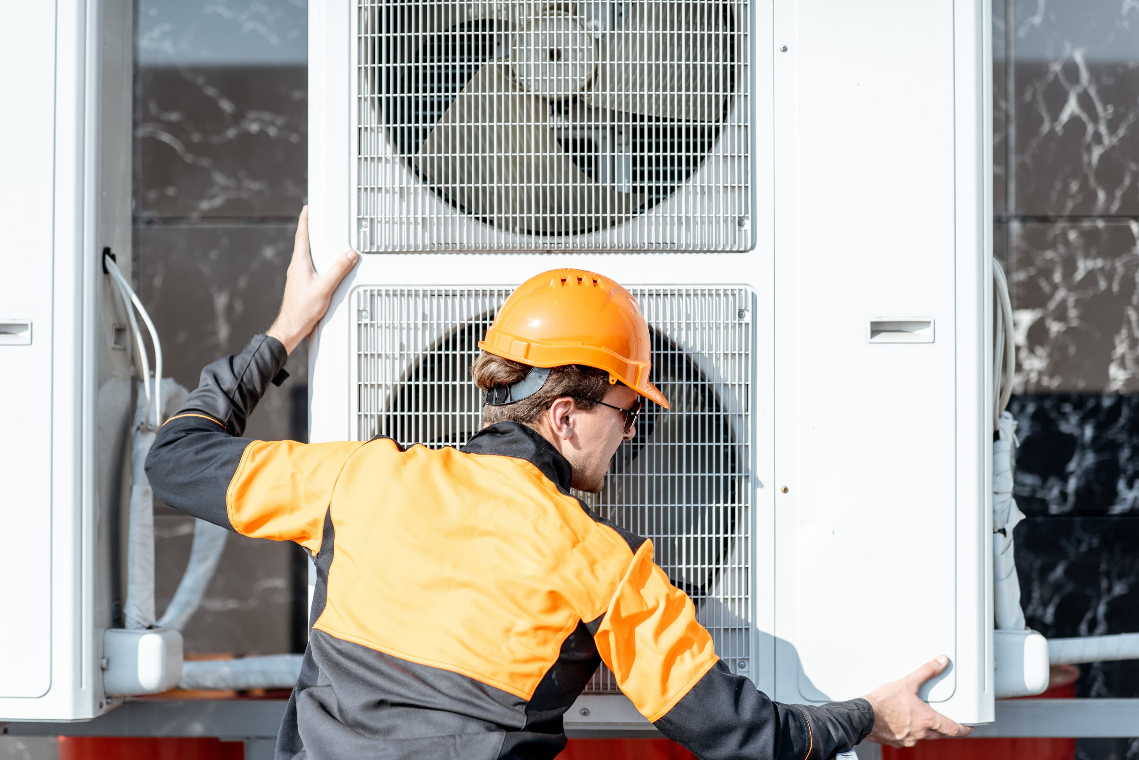 HVAC technician wearing an orange helmet servicing outdoor air conditioning unit.