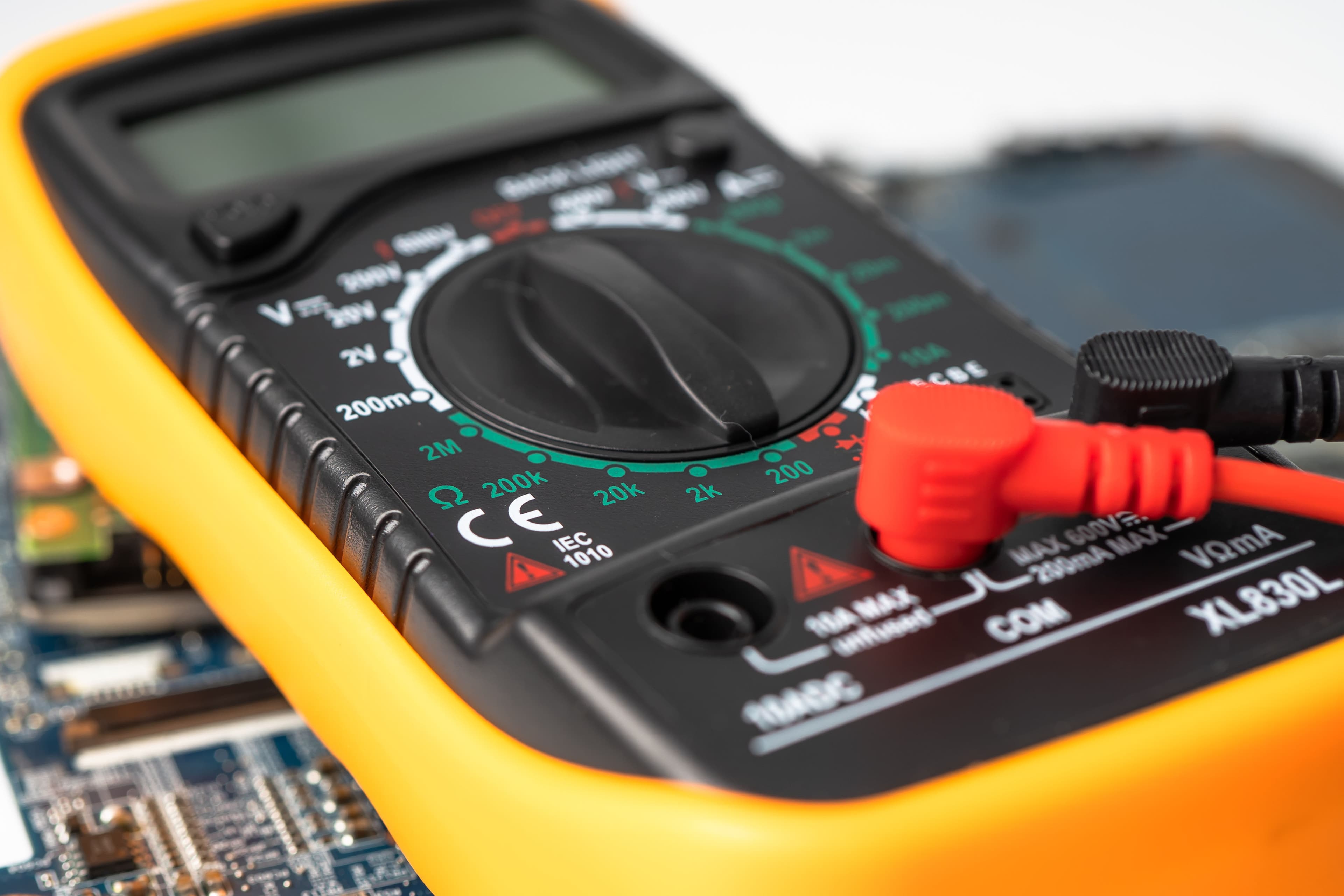 Digital multimeter with red and black probes on a circuit board background.