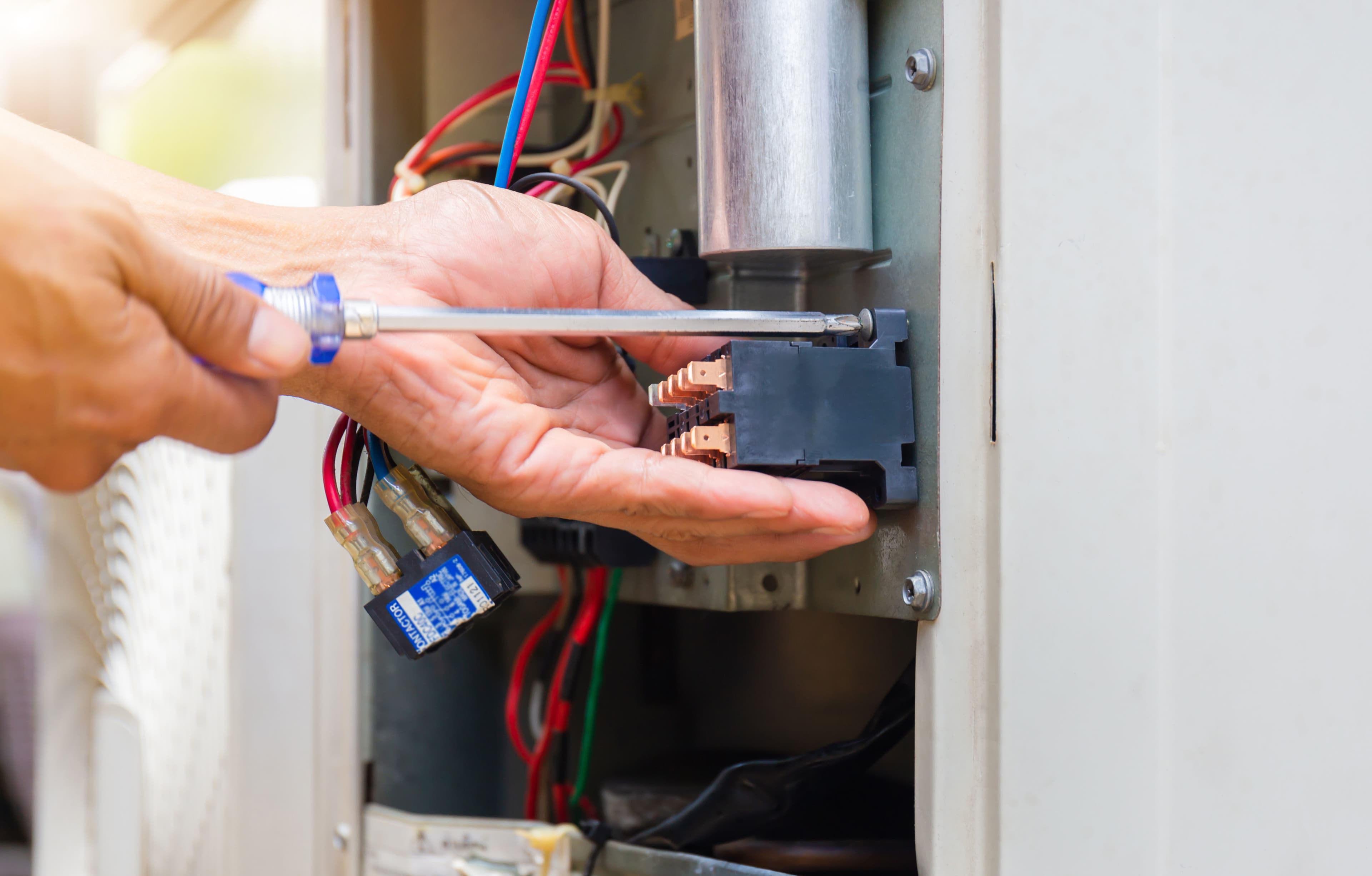 Person using a screwdriver to repair electrical connections inside an appliance.