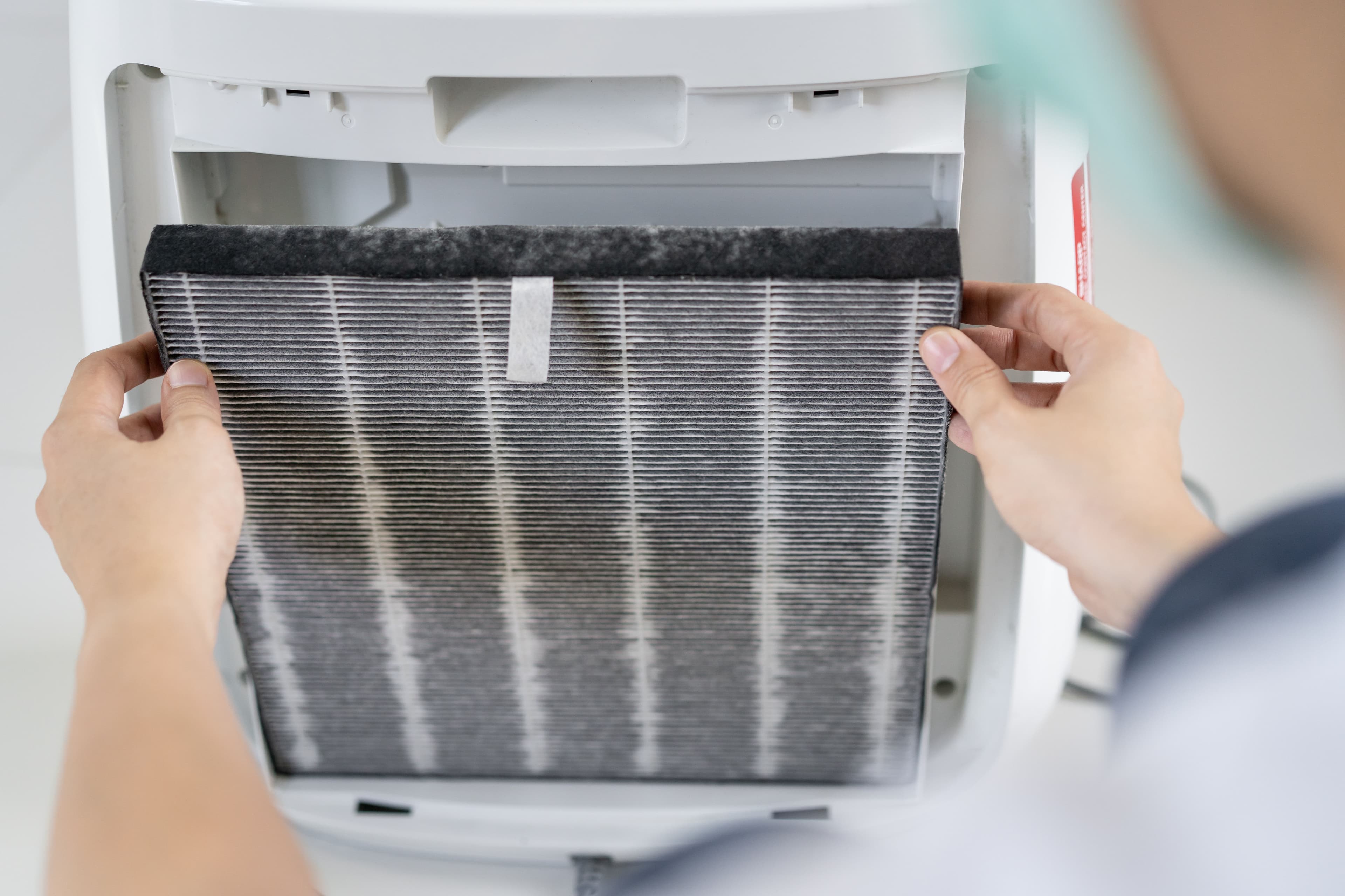 Person replacing a filter in an air purifier, highlighting maintenance for better air quality.