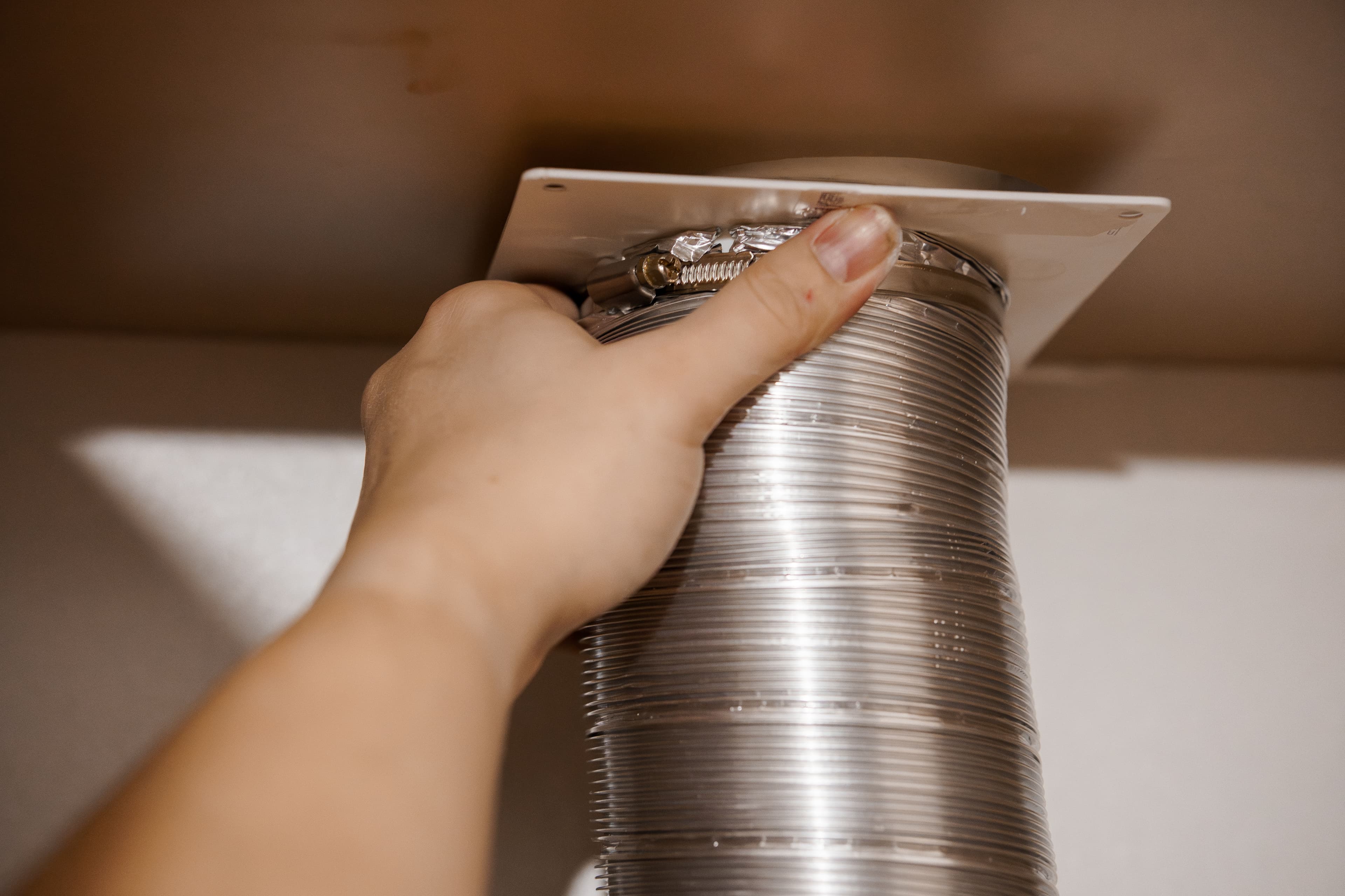 Hand connecting aluminum duct to ceiling vent for proper ventilation installation.