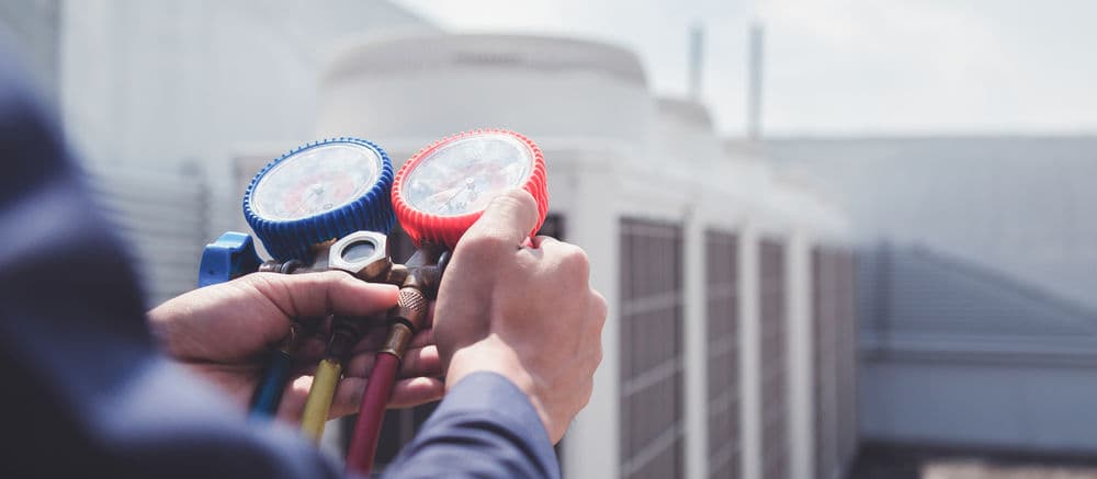 Technician using refrigerant gauges on HVAC system outdoors for maintenance or repair.