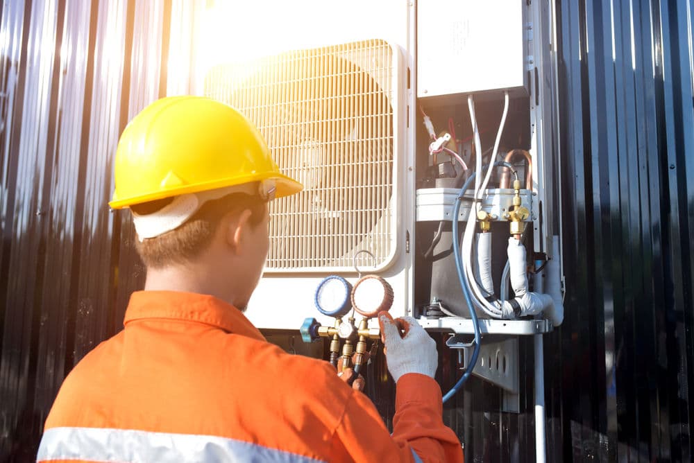 HVAC technician in safety gear checking air conditioning unit outdoors.