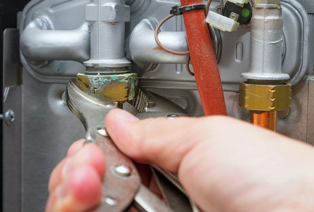 Person using pliers to tighten a valve on a plumbing pipe system.