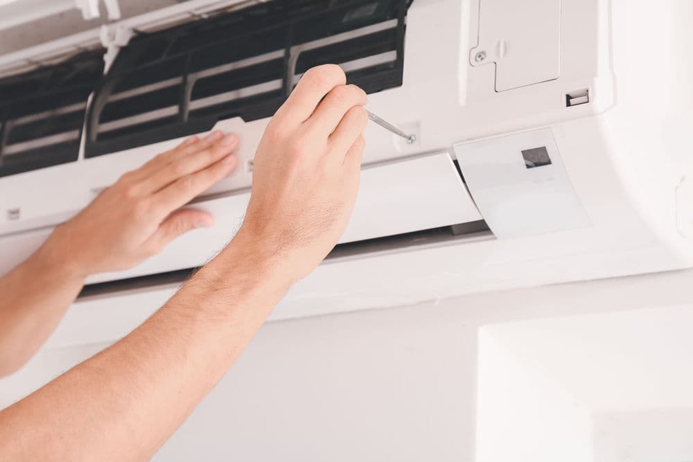 Person servicing a wall-mounted air conditioner with a screwdriver.